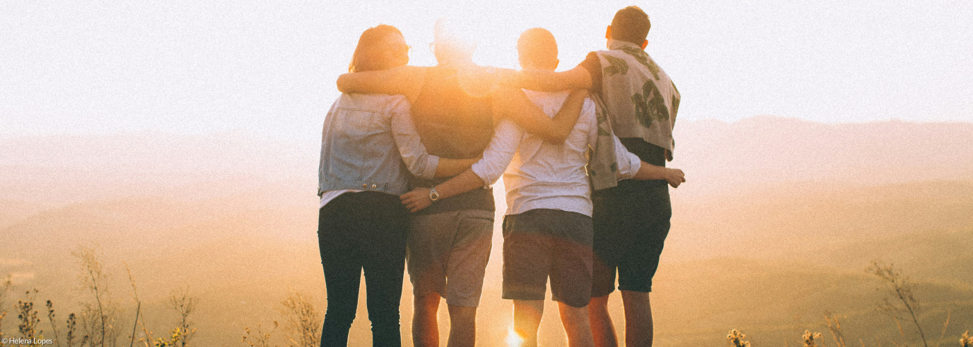 Junge Menschen stehen im Sonnenuntergang Arm in Arm